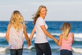 Lucy Good holds hands with her two daughters on the beach