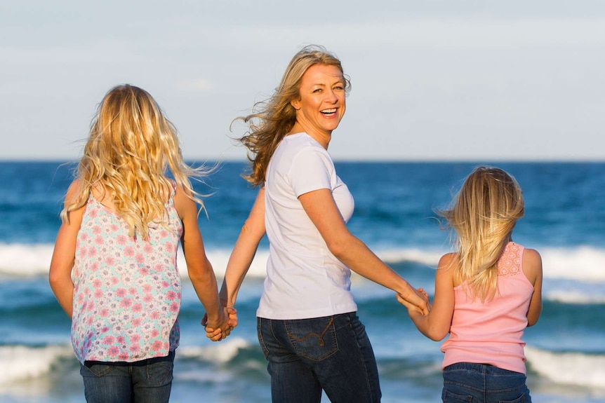 Lucy Good holds hands with her two daughters on the beach