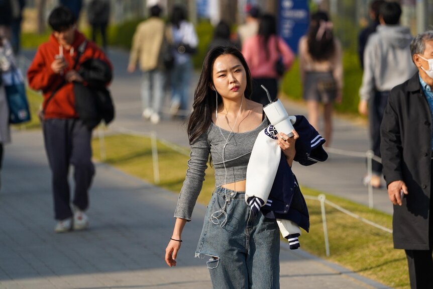 A woman wearing a grey top and pants holds a waterbottle as she walks down a path.