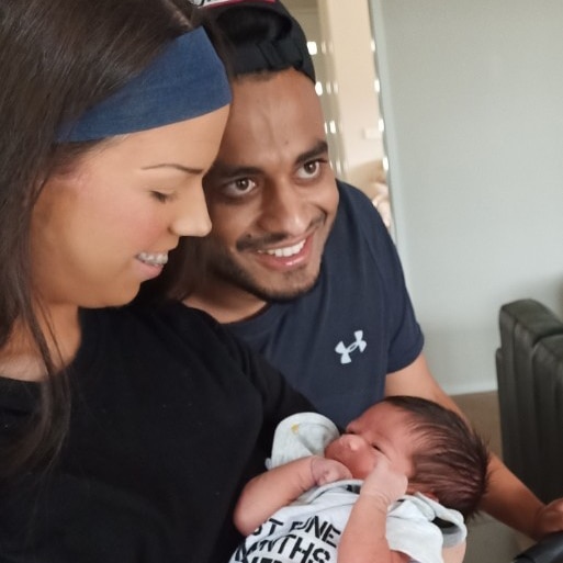 A young woman holding a baby and smiling, next to her partner who is also smiling.