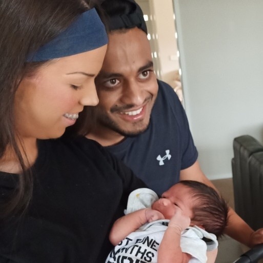 A young woman holding a baby and smiling, next to her partner who is also smiling.