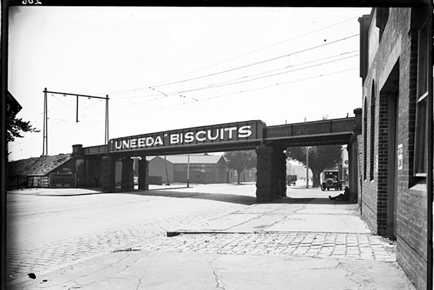 Black and white photo of light rail bridge, with ad for Uneeda Biscuits