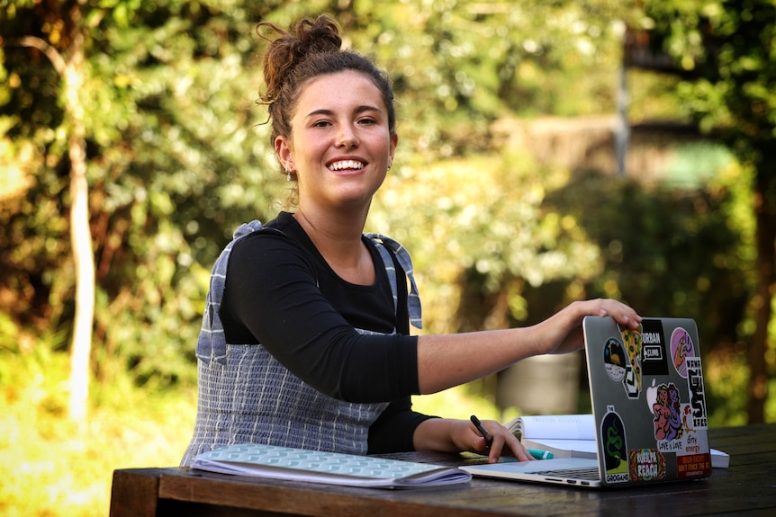 Lily Kerley with her hair up, sitting at a table outside with her laptop open in front of her.