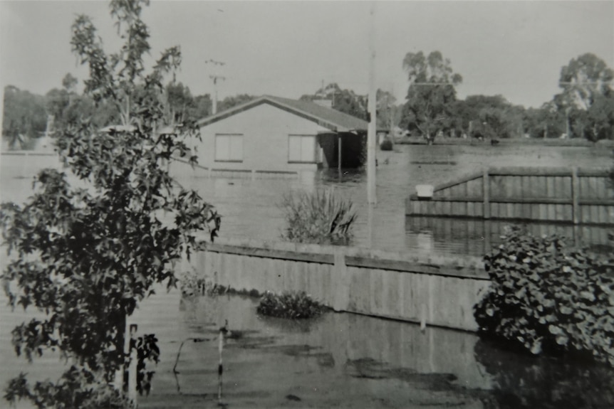 A black and white photo shows a house half submerged in water.