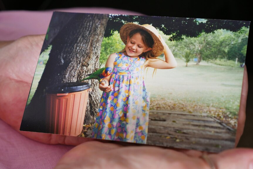A young girl wearing a colourful dress with a rainbow lorikeet on her arm.