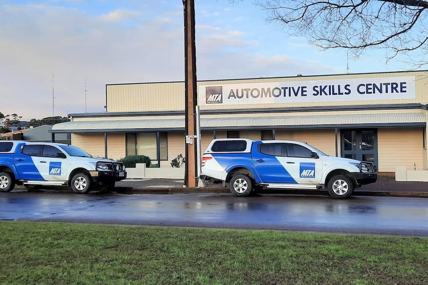 Street view of two cars outside of building with sign Automotive Skills Centre
