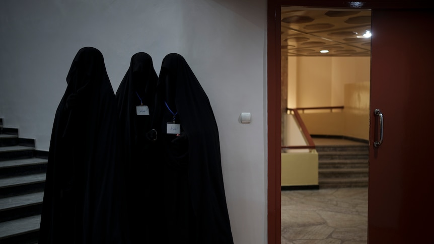 Three women stand in burkas inside a university auditorium