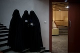 Three women stand in burkas inside a university auditorium