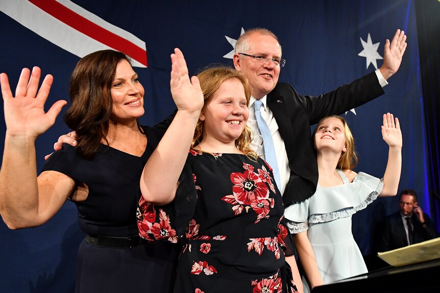 Scott Morrison flanked by his wife and two daughters wave to supporters after his victory speech