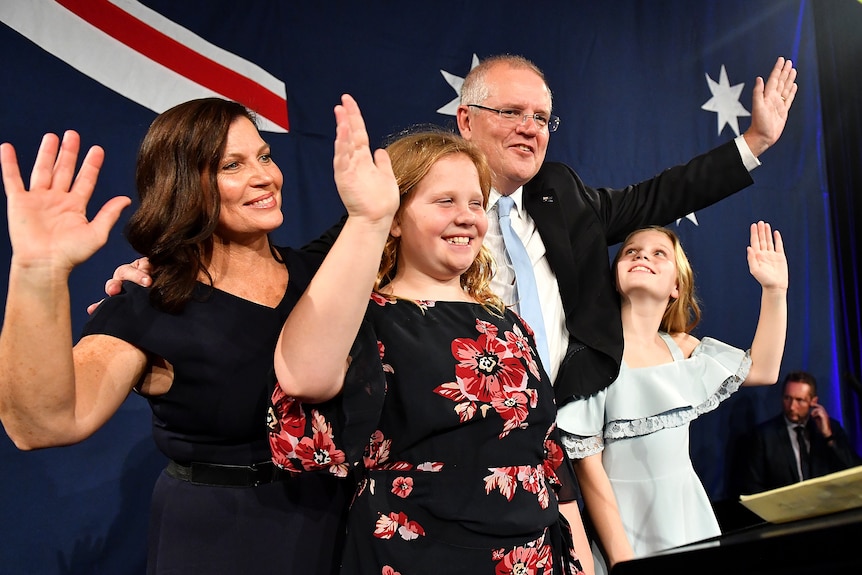 Scott Morrison flanked by his wife and two daughters wave to supporters after his victory speech