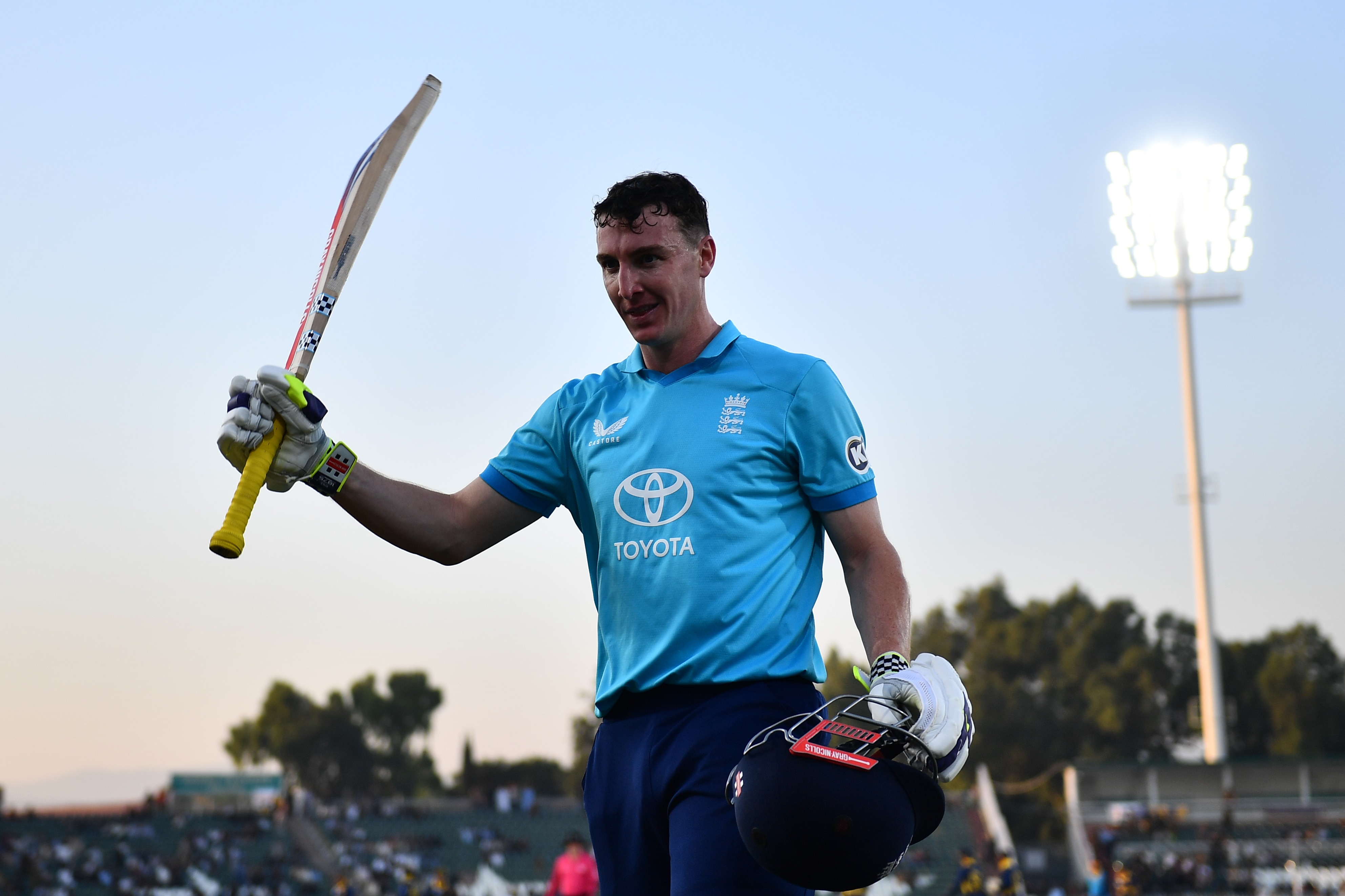 Harry Brook raises bat with right hand holds helmet in left