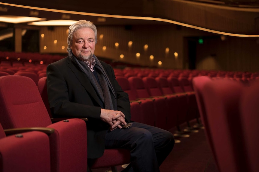 Douglas Gautier is seated inside an empty theatre.