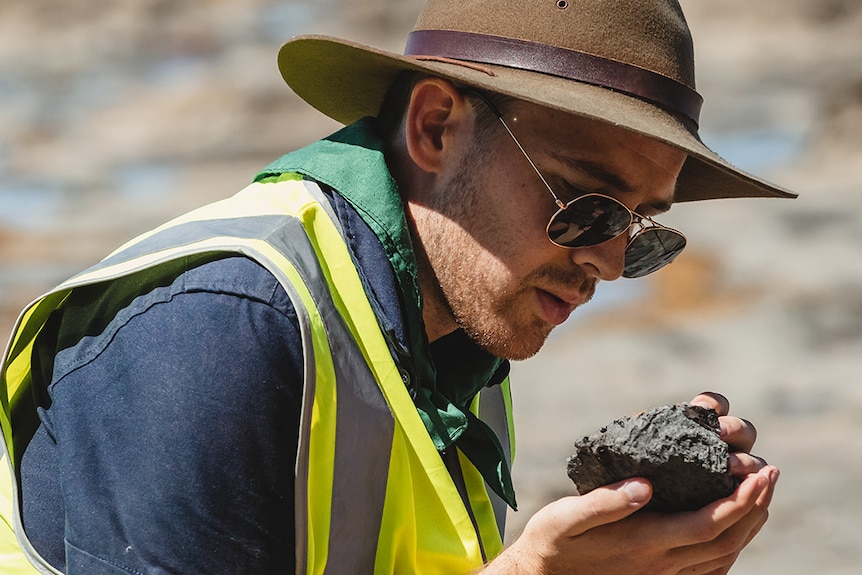 A young man looking at a fossil specimen in the field wearing a hat