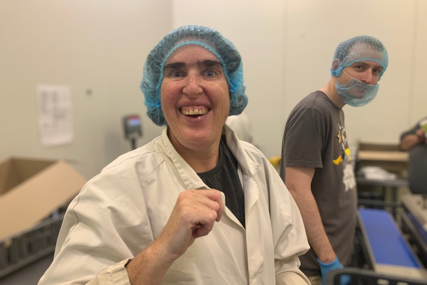 In white coat and protective hair net, a smiling woman works at a packaging plant