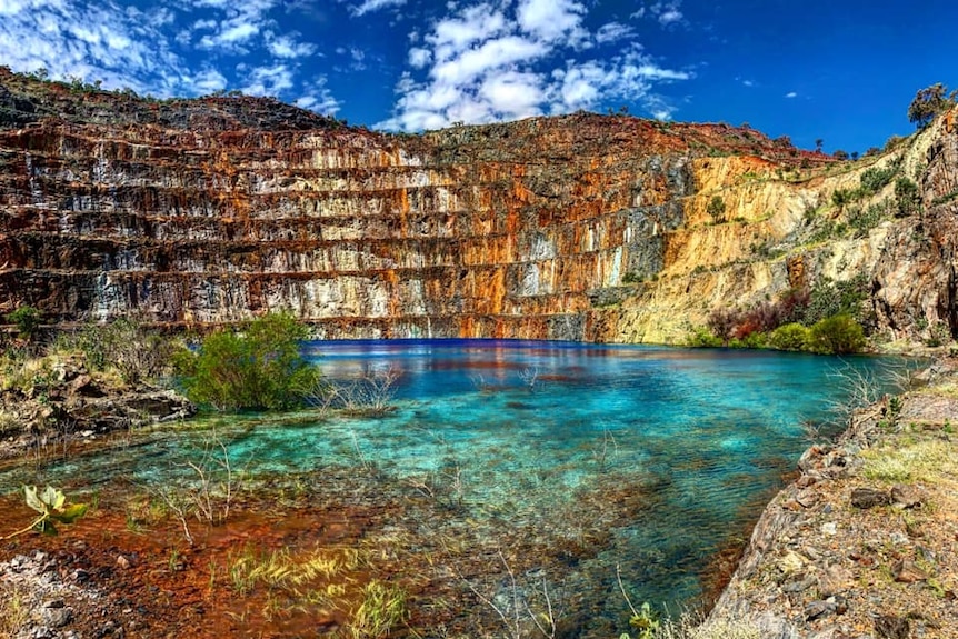 A photo of a landscape of an old mine, with stunning blue water in a dam.