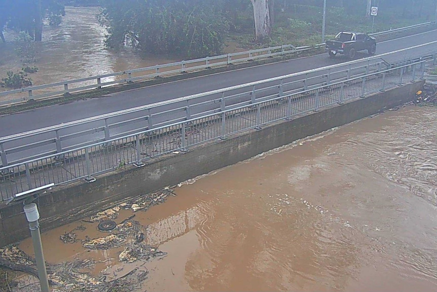 Brown water rising up a bridge. A ute driving across left to right. 