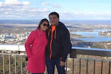 A man and woman stand at a lookout with an expansive view of Canberra behind them.