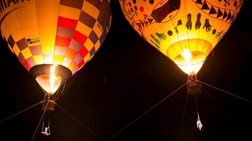 Trapeze artists perform under two hot air balloons.