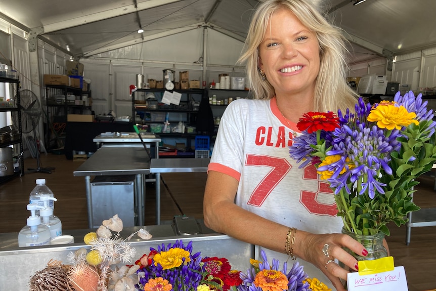 smiling woman holding bunches of flowers inside makeshift kitchen inside a marquee