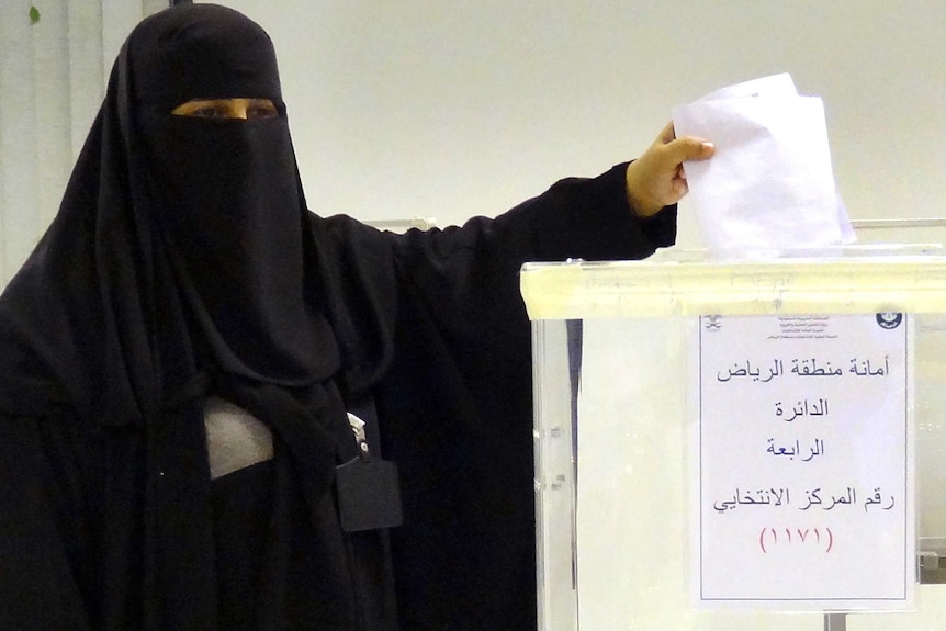 A Saudi woman places her vote into a ballot box.