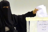 A Saudi woman places her vote into a ballot box.