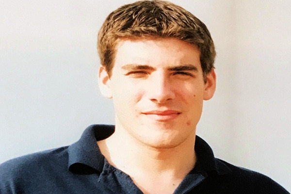 A photograph of an approximately 20-year-old man with short brown hair wearing a navy blue polo shirt.