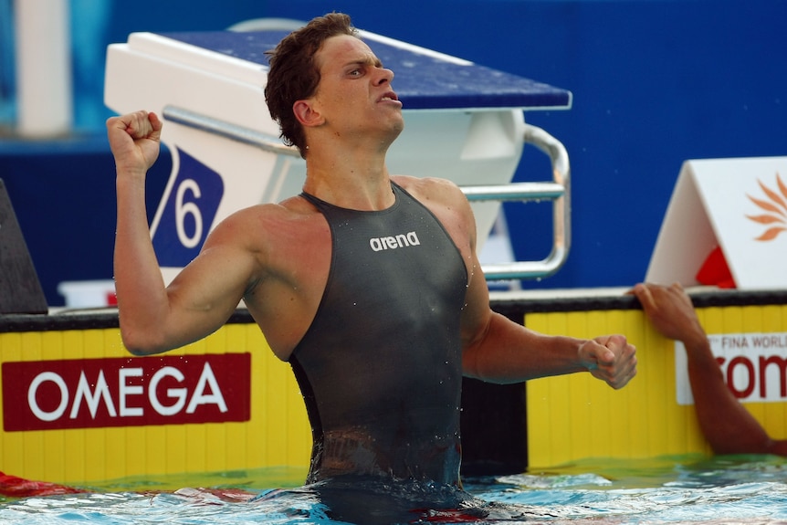 A man wearing a full-body swim suit punches the air with delight after breaking a world record.
