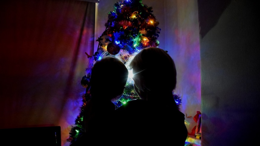 Two people in front of a lit Christmas tree.