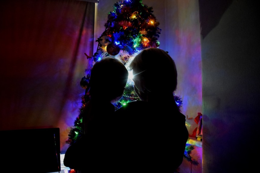 Two people in front of a lit Christmas tree.