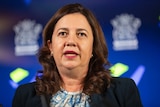 Ms Palaszczuk speaks at a press conference in front of a blue screen with the Queensland government logo.
