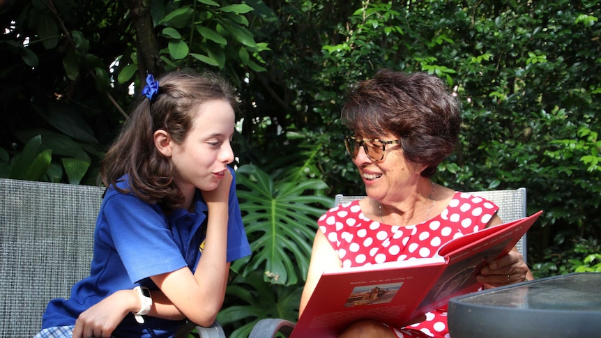 A child in a school uniform leans over as she is read to by her grandmother