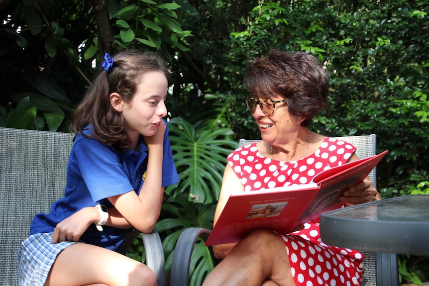 A child in a school uniform leans over as she is read to by her grandmother