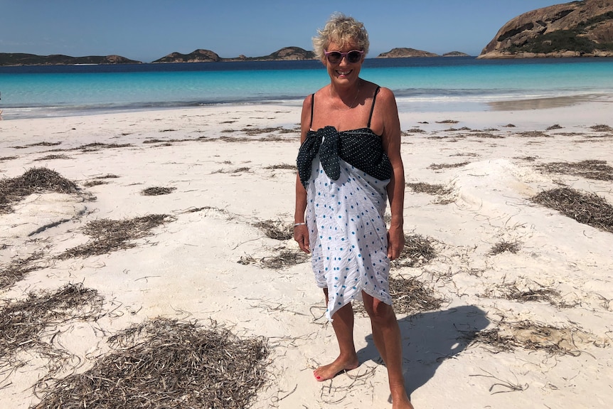 Beach view on sunny day, white sands, clear waters and woman dressed in swimwear and sunglasses in foreground