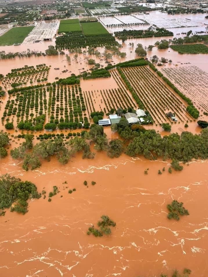 Aerial shot of trees and farms in floodwater stretching to the horizon from the overflowing banks of a muddy brown river.