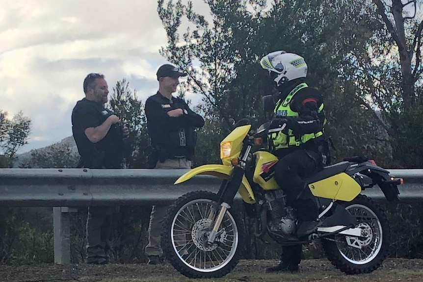 Two police officers talk to another officer who is on a motorbike on the side of the road