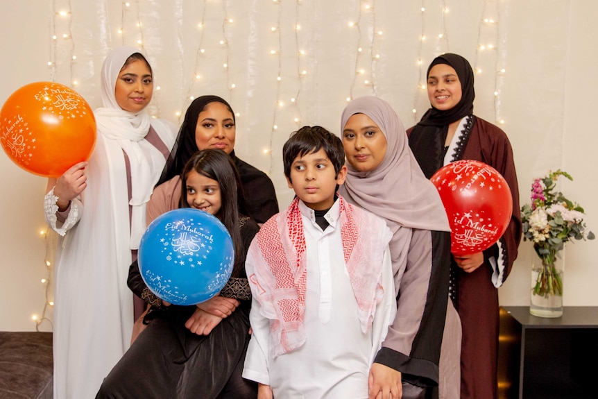 A group photos of siblings with balloons and light decorations at the background