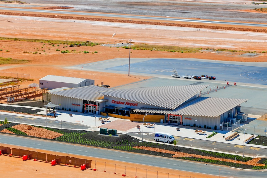An aerial view of the terminal and runway at a regional airport, surrounded by red dust. One van is parked in front.