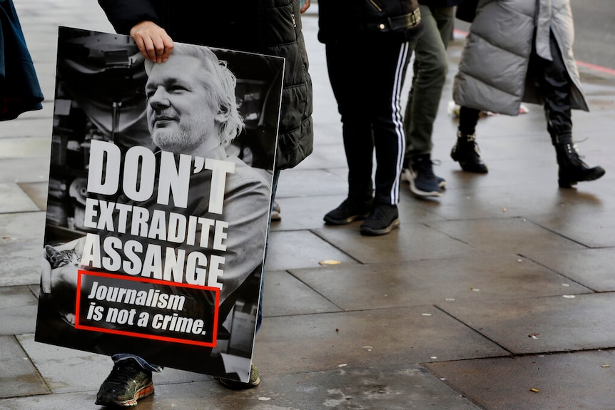 A protester holds a sign showing Julian Assange's face with a slogan.