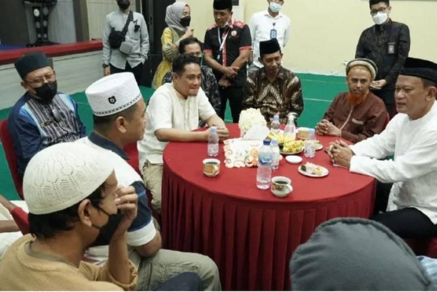 A group of men sit around a table at an event mostly dressed in Islamic attire.