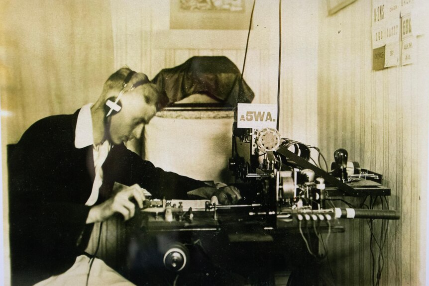 A black and white photo of a man with headphones using radio equipment.