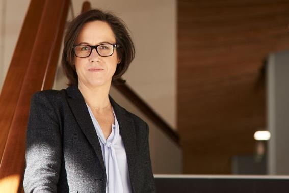 A portrait photo of a woman in a grey suit jacket and glasses.