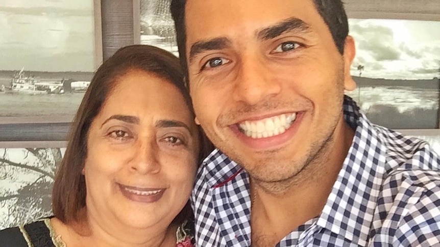 A woman we with shoulder length hair, smiling and wearing a floral shirt next to her son, with a huge smile, dark hair.