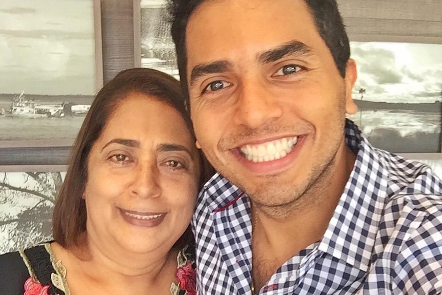 A woman we with shoulder length hair, smiling and wearing a floral shirt next to her son, with a huge smile, dark hair.