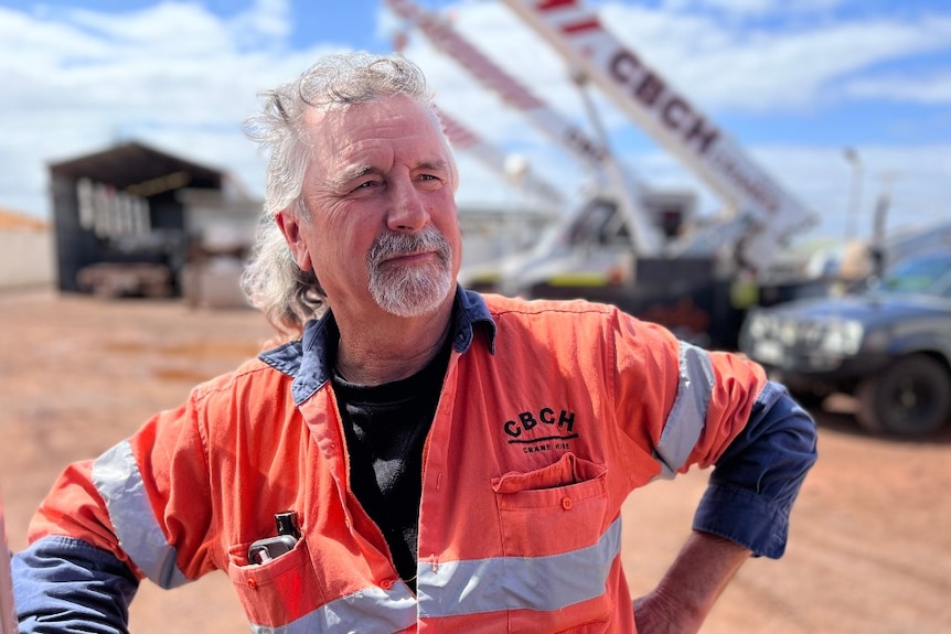 A middle-aged man in high-vis stands in front of a crane.