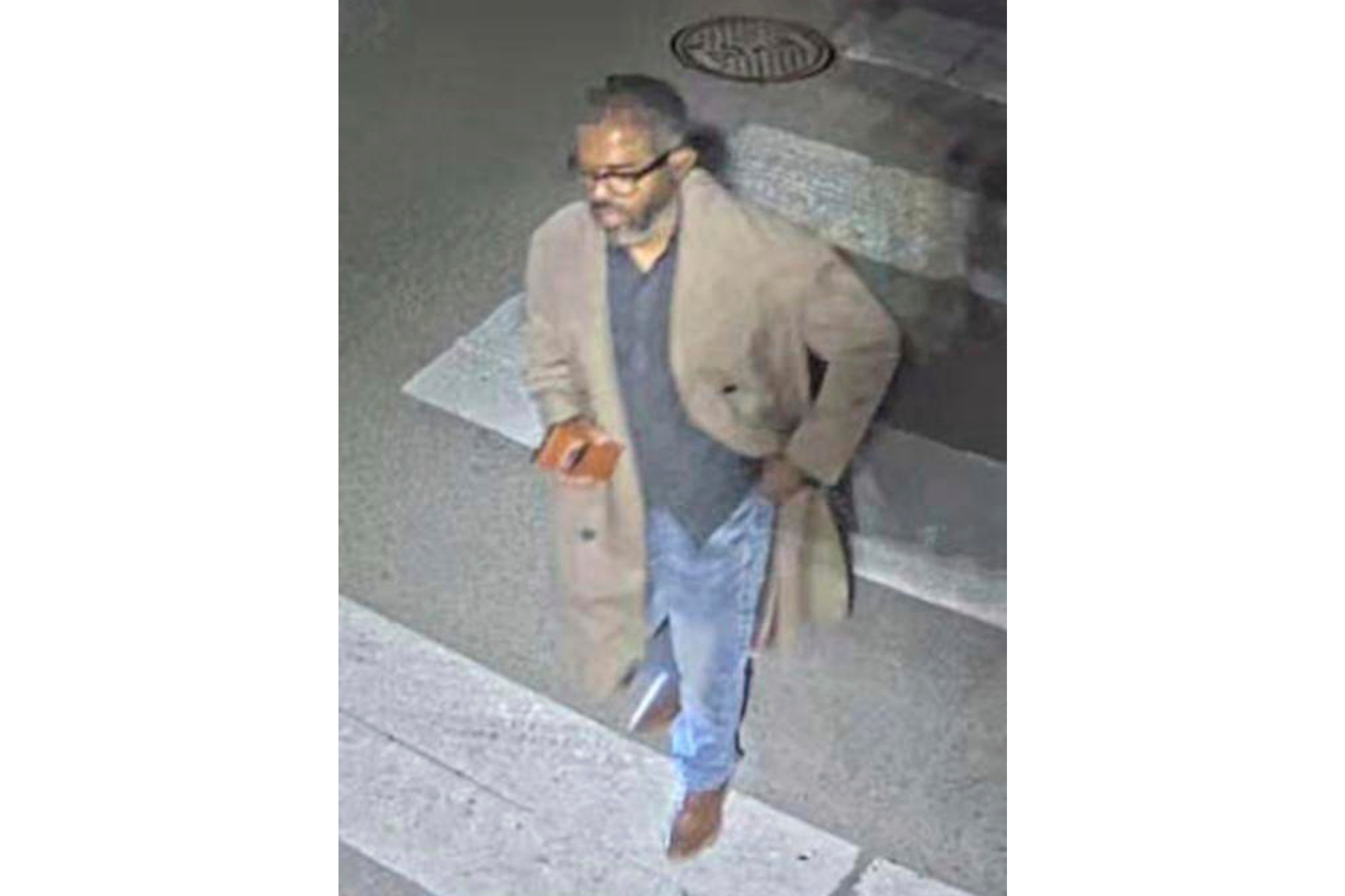 A black man in jeans, a long coat and glasses is seen crossing a road in a CCTV image