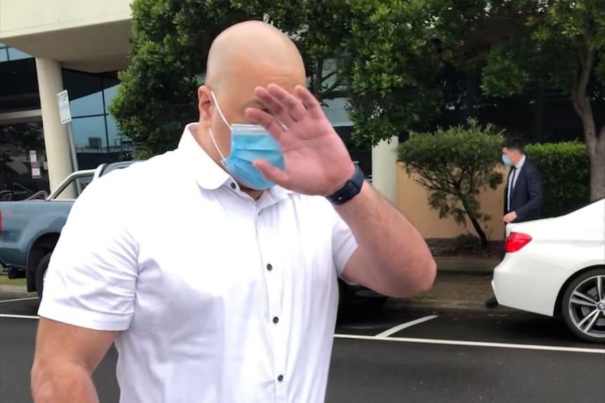 bald man with white button up t-shirt covers his face with hand as he leaves court