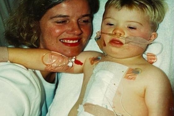 young boy lays on hospital bed with mum and tubes coming from nose