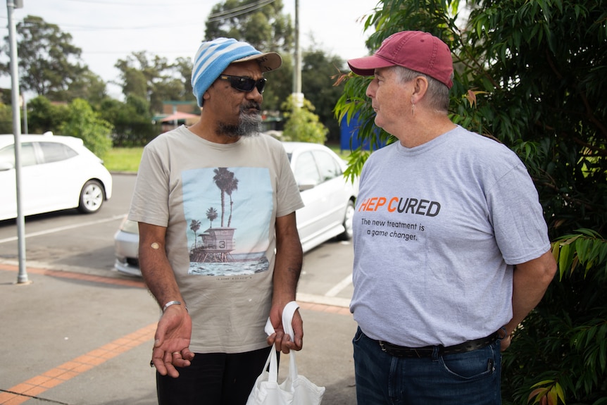 a man wearing dark glasses talking with a man wearing a cap and looking at thim