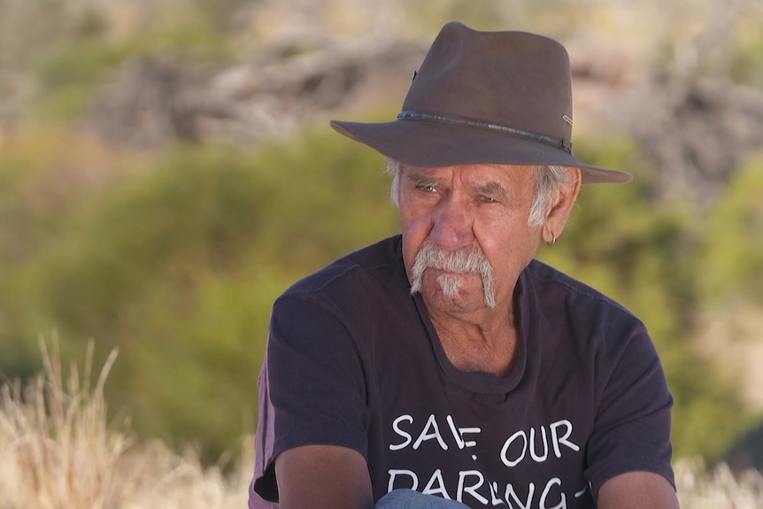 Indigenous man wearing a t-shirt and hat looking at an interviewer.