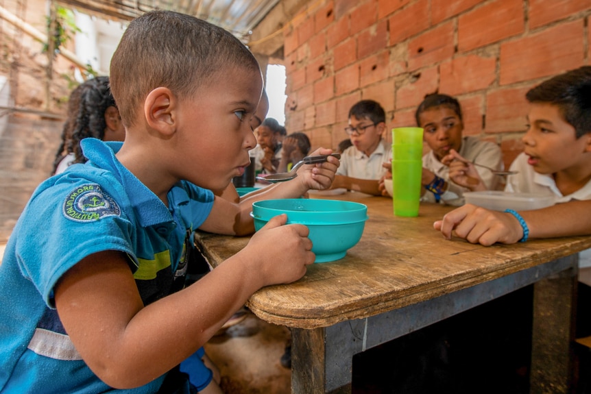A little Venezuelan boy eating from bright blue plastic bowl